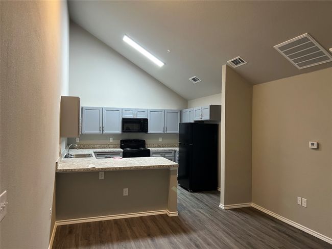 Kitchen with black appliances, a peninsula, vaulted ceiling, light countertops, and dark wood-style floors | Image 6