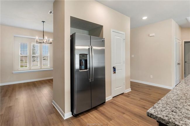 Kitchen featuring stainless steel refrigerator with ice dispenser, light wood-style flooring, a chandelier, light stone counters, and recessed lighting | Image 11