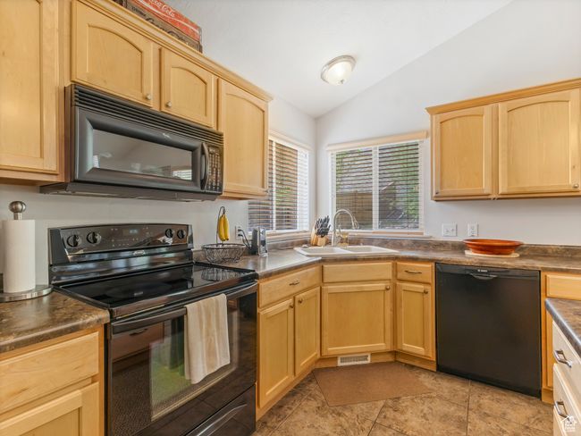 Kitchen with black appliances, a sink, lofted ceiling, light brown cabinetry, and dark countertops | Image 13