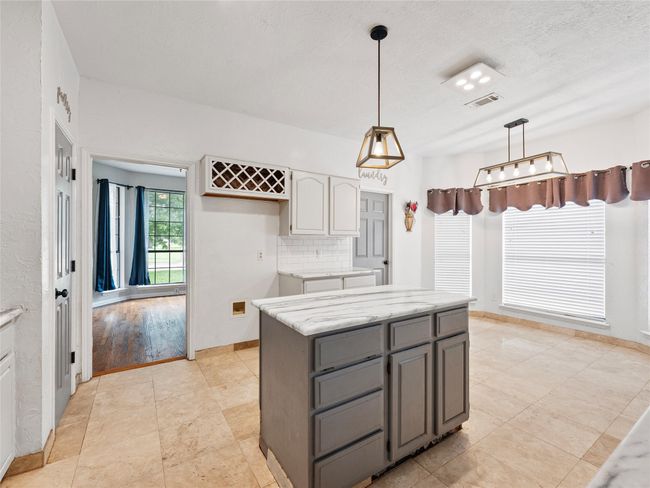 Kitchen featuring gray cabinetry, hanging light fixtures, a center island, backsplash, and light stone counters | Image 11