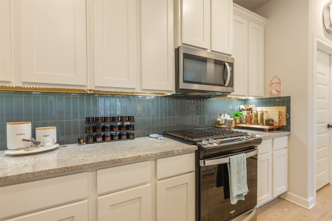 Kitchen featuring appliances with stainless steel finishes, backsplash, white cabinetry, and light stone counters | Image 13