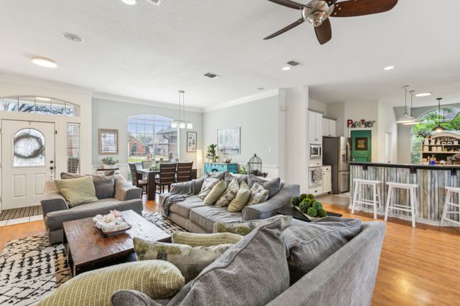 Living room with light wood-type flooring, a ceiling fan, ornamental molding, and visible vents | Image 9
