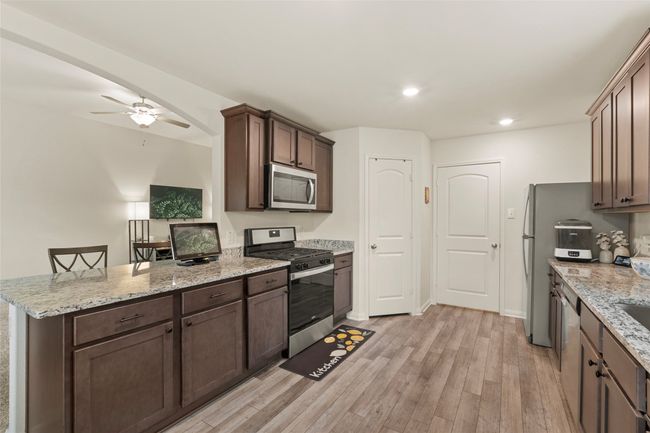 Kitchen with light granite countertop, dark brown cabinetry, luxury vinyl plank flooring, and stainless steel appliances | Image 9