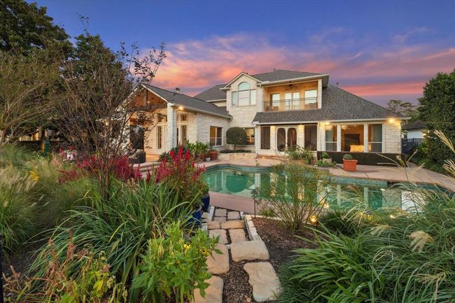 This beautiful two-story home features a stone exterior, a spacious backyard with a pool, lush landscaping, and a covered patio, perfect for outdoor entertaining. The sunset sky adds a picturesque backdrop. | Image 34