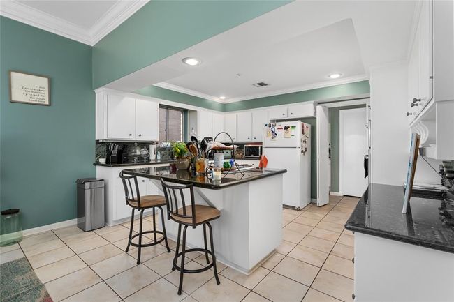 This spacious kitchen features a large central island with bar seating, providing both functionality and a casual dining option. The white cabinetry offers ample storage, while the granite countertops add a sleek and polished touch. Recessed lighting and crown molding enhance the space, creating a bright and inviting atmosphere. | Image 20