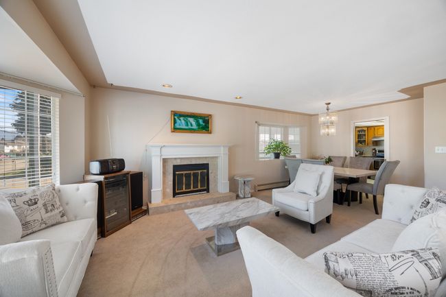 Living room featuring a high end fireplace, a notable chandelier, baseboard heating, and light colored carpet | Image 13