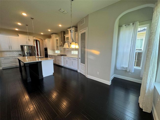 Kitchen with arched walkways, fridge with ice dispenser, stainless steel gas cooktop, wall chimney exhaust hood, and dark wood-style floors | Image 18
