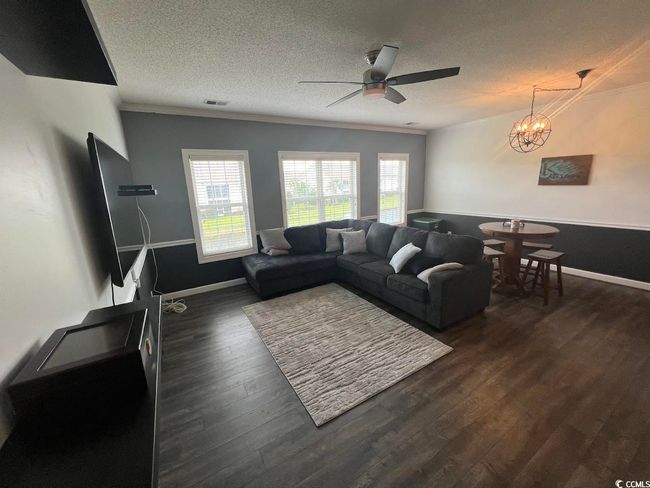 Living area featuring ceiling fan, a textured ceiling, ornamental molding, dark wood-style floors, and a chandelier | Image 6