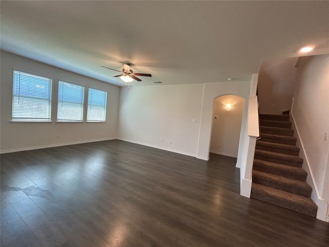 Unfurnished living room featuring arched walkways, a ceiling fan, dark wood-style floors, stairway, and baseboards | Image 8