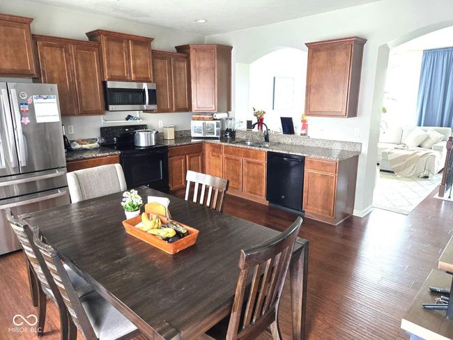 kitchen with black appliances, arched walkways, dark wood-style flooring, brown cabinets, and recessed lighting | Image 6
