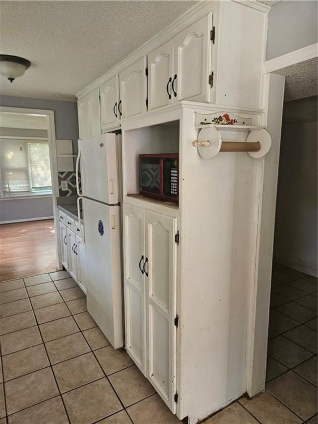 Kitchen featuring fridge, a textured ceiling, light tile patterned floors, and white cabinetry | Image 6