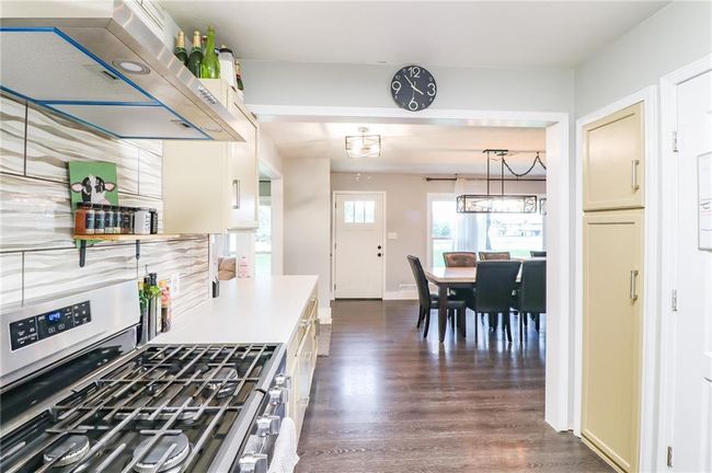 Kitchen featuring stainless steel gas range oven, wall chimney range hood, dark wood-style flooring, light countertops, and hanging light fixtures | Image 9