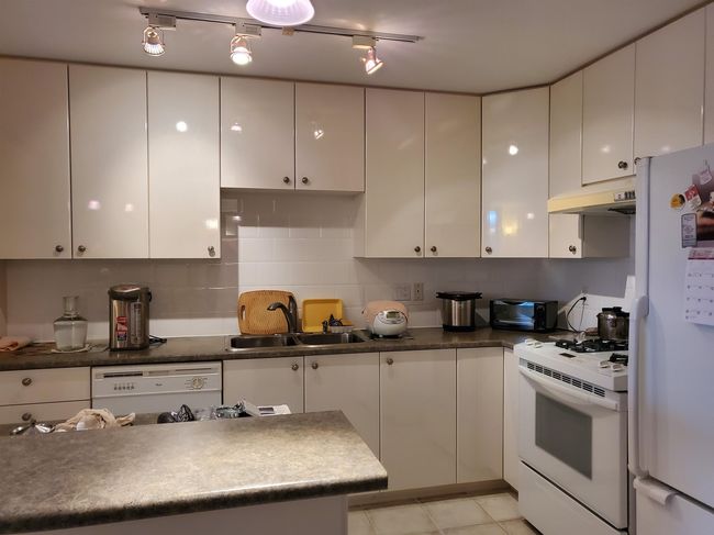 Kitchen featuring white cabinetry, white appliances, under cabinet range hood, and a sink | Image 10