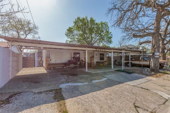 Back of property featuring stone siding, fence, concrete driveway, and a carport | Image 7