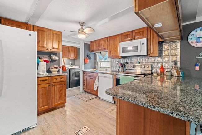 Kitchen with tasteful backsplash, dark stone countertops, light hardwood / wood-style floors, white appliances, and washer / dryer | Image 11