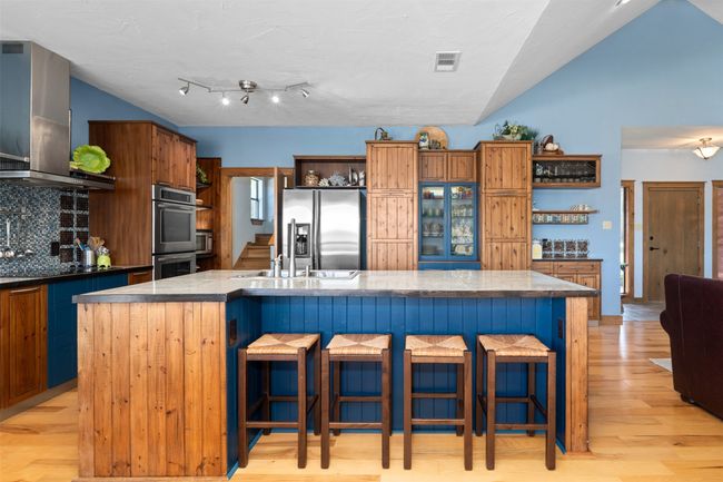 Kitchen with wall chimney range hood, appliances with stainless steel finishes, tasteful backsplash, and an island with sink | Image 9