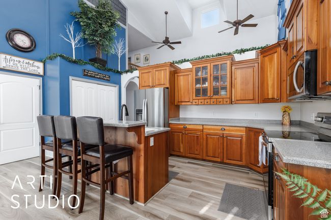Kitchen with appliances with stainless steel finishes, high vaulted ceiling, a ceiling fan, brown cabinetry, and a breakfast bar area | Image 14