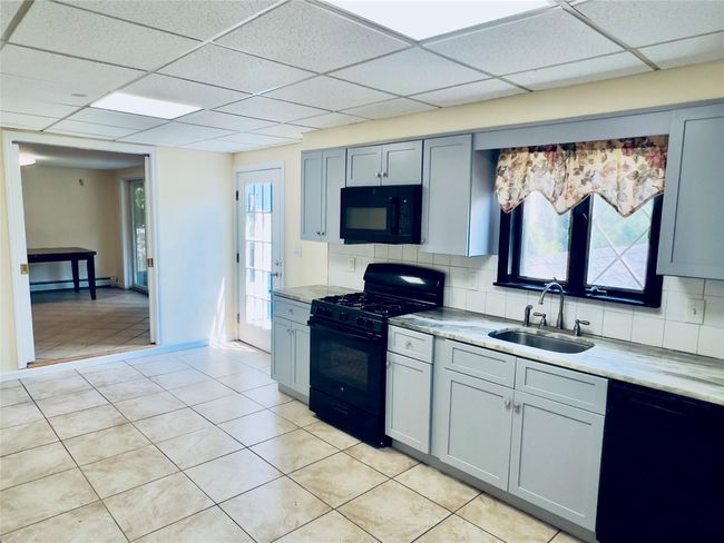 Kitchen with black appliances, a paneled ceiling, tasteful backsplash, light tile patterned floors, and a baseboard heating unit | Image 7
