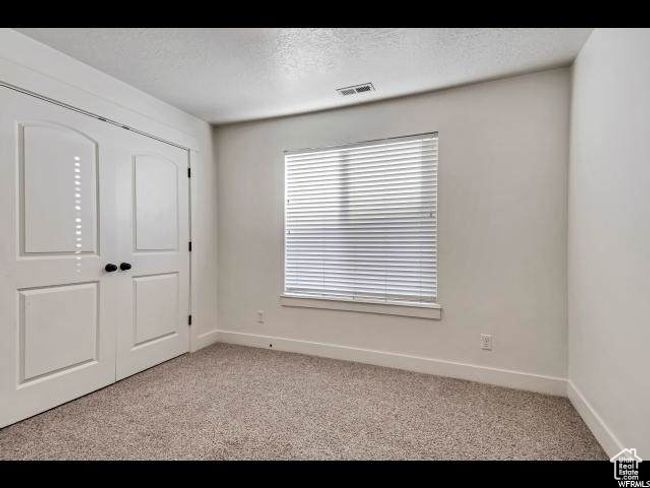 Unfurnished bedroom with light colored carpet, baseboards, a textured ceiling, and a closet | Image 9