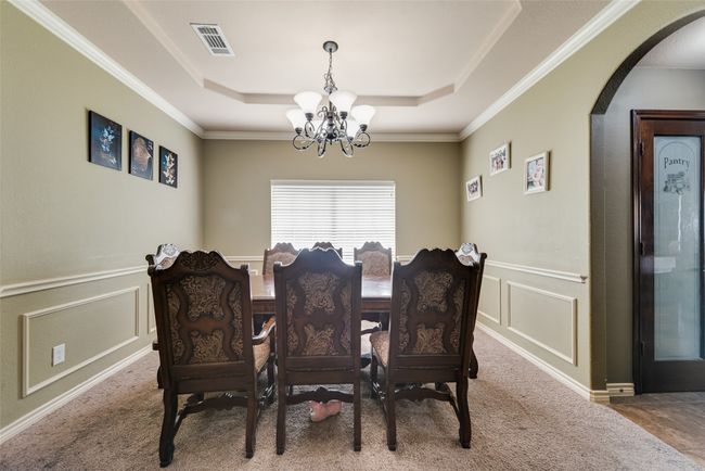 Carpeted dining room with a chandelier, a raised ceiling, arched walkways, a decorative wall, and ornamental molding | Image 5