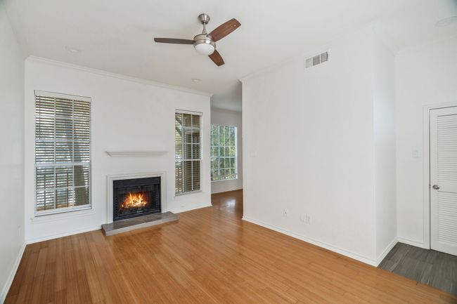 Unfurnished living room featuring crown molding, wood finished floors, a glass covered fireplace, ceiling fan, and visible vents | Image 5