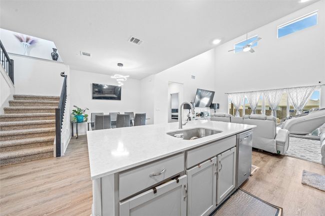 Kitchen with light wood-style floors, stainless steel dishwasher, light countertops, a sink, and open floor plan | Image 11