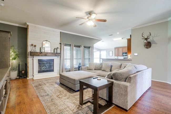 Living area featuring a ceiling fan, wood finished floors, a fireplace, ornamental molding, and baseboards | Image 15