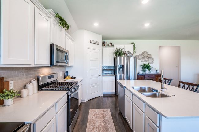 Kitchen featuring stainless steel appliances, dark wood finished floors, backsplash, white cabinets, and light countertops | Image 14