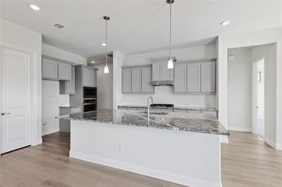 Kitchen featuring appliances with stainless steel finishes, a kitchen island with sink, dark stone counters, light wood-type flooring, and decorative light fixtures | Image 3