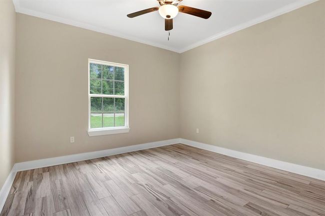 This room features neutral-toned walls, wood-look flooring, and a ceiling fan. A large window allows natural light to illuminate the space, creating a bright and airy atmosphere. Perfect for a bedroom or home office. | Image 14