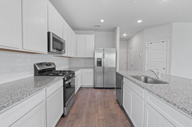 Kitchen with appliances with stainless steel finishes, white cabinetry, dark wood-style floors, light stone counters, and recessed lighting | Image 11
