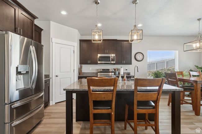 Kitchen with appliances with stainless steel finishes, dark brown cabinetry, light wood-style flooring, recessed lighting, and a kitchen breakfast bar | Image 15