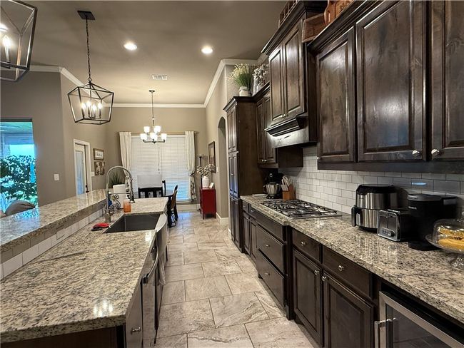 Kitchen with tasteful backsplash, crown molding, light stone counters, stone tile floors, and a chandelier | Image 7