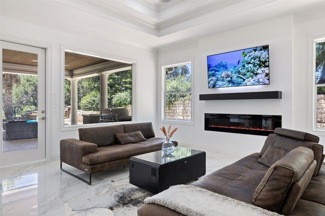 Living area with marble tiled floors, healthy amount of natural light, crown molding, a glass covered fireplace, and a tray ceiling | Image 13