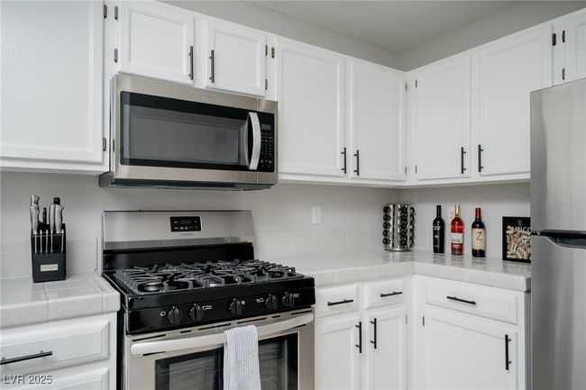 Kitchen with tile counters, stainless steel appliances, and white cabinets | Image 11