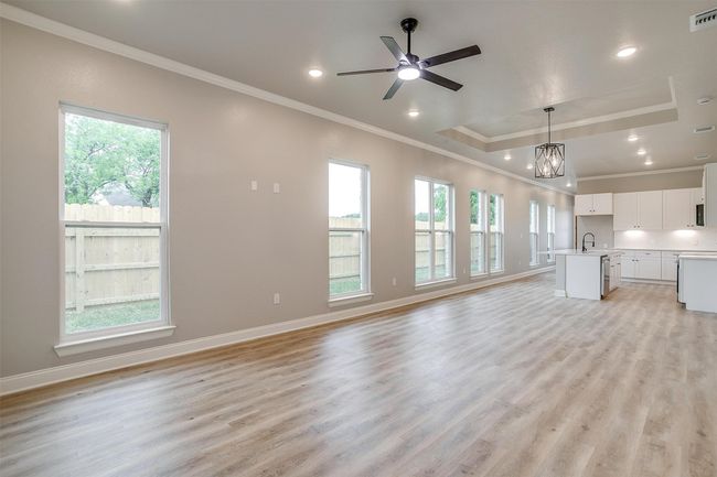 Unfurnished living room featuring a sink, ornamental molding, a tray ceiling, and light wood-type flooring | Image 8