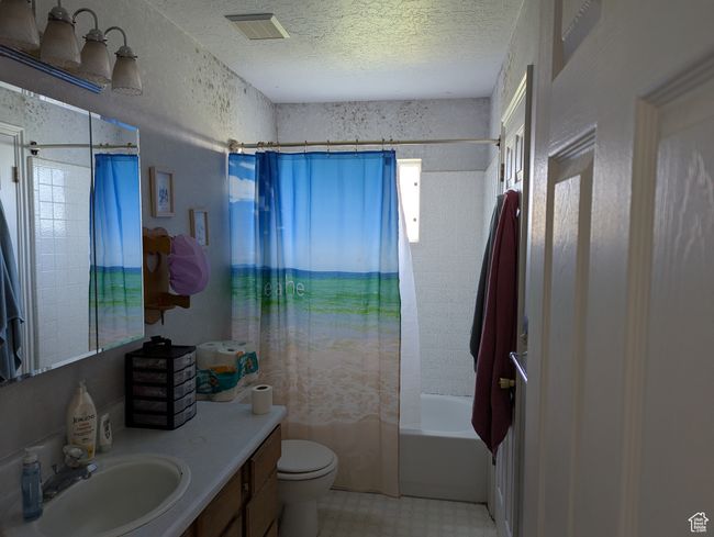 Full bath with a textured ceiling, vanity, shower / bath combination with curtain, toilet, and visible vents | Image 5