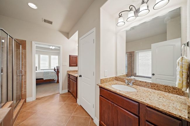 Bright and spacious bathroom with a large mirror, granite countertop, and stylish lighting. Features a glass-enclosed shower and access to a cozy bedroom with ample natural light. | Image 22