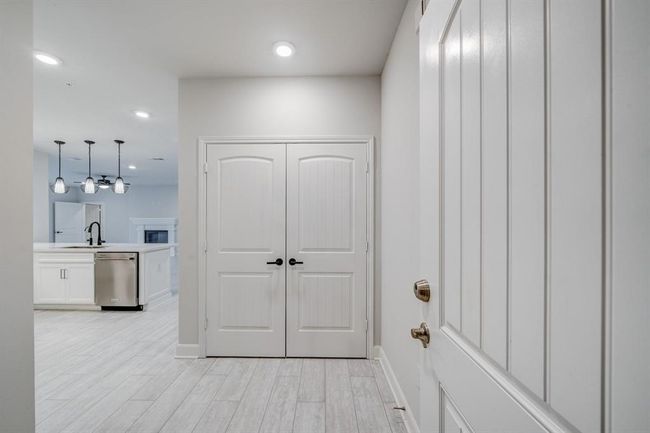 Bright and modern entryway leading into an open-concept kitchen and living space. Features light wood flooring, sleek white cabinetry, and stylish pendant lighting. | Image 23