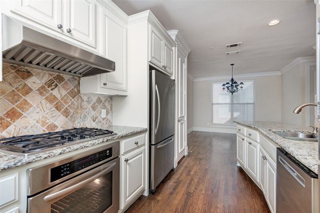 Kitchen featuring stainless steel appliances, under cabinet range hood, white cabinetry, a chandelier, and decorative backsplash | Image 6