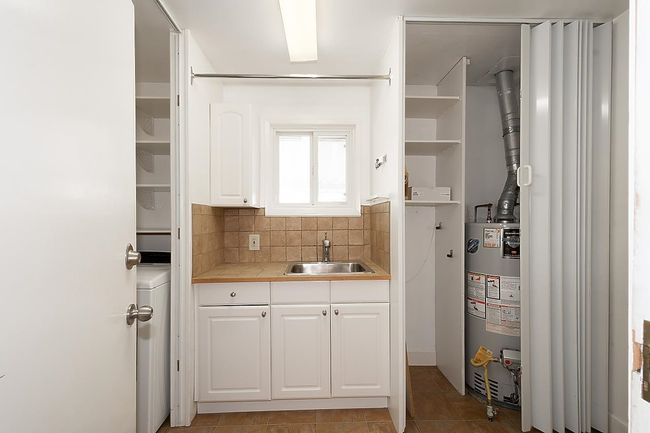 Kitchen featuring gas water heater, white cabinets, light countertops, and backsplash | Image 22