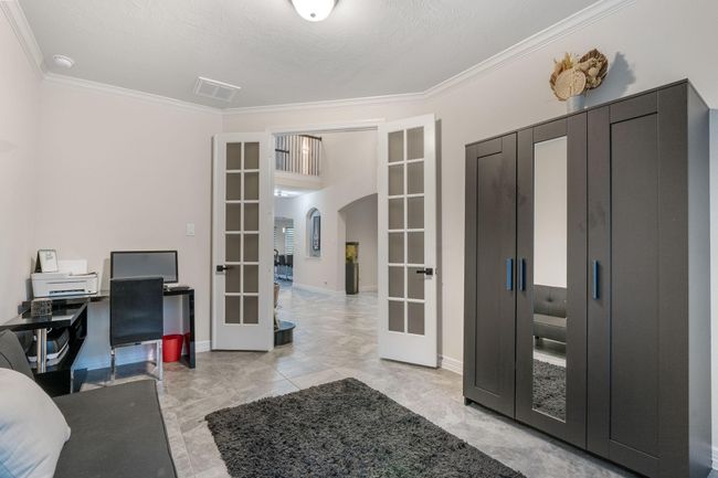 This room features a modern work space French doors leading to an open hallway. The neutral walls and tile flooring create a clean, inviting atmosphere. | Image 7