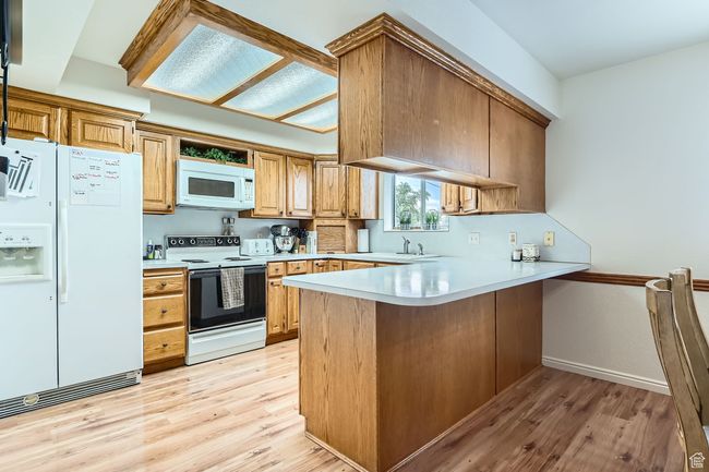 Kitchen featuring white appliances, a peninsula, light wood-style flooring, and light countertops | Image 4