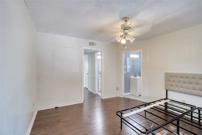 Unfurnished bedroom with wood finished floors, a textured ceiling, ensuite bathroom, and ceiling fan | Image 5