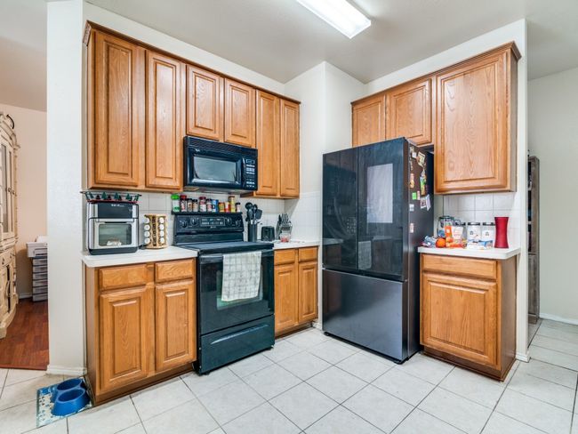 Kitchen with backsplash, black appliances, brown cabinets, light countertops, and light tile patterned floors | Image 11