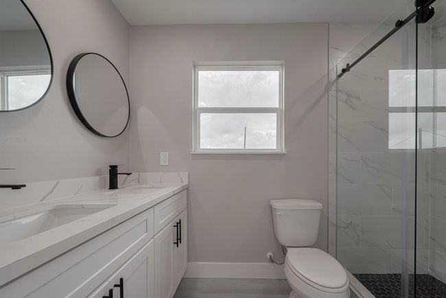 Stylish and serene, this bath features a glass-enclosed shower with full-height tilework, a dual-sink vanity with black fixtures, and a window that fills the space with natural light. | Image 17