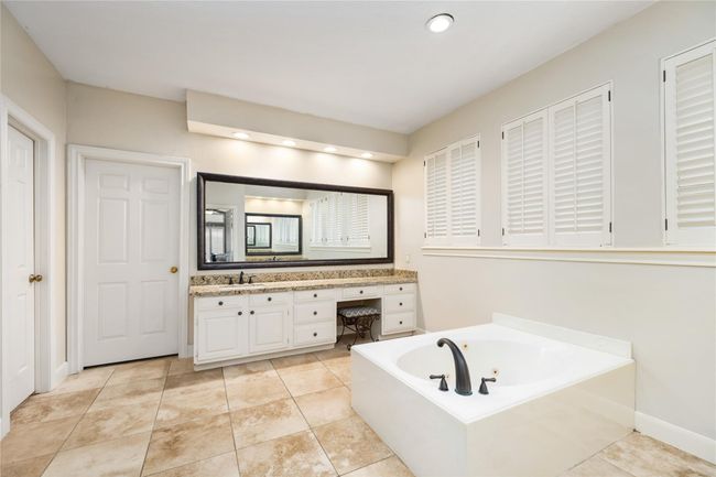The en-suite bath is expansive and thoughtfully designed, with windows adorned in shutter-style blinds, dual sinks, granite counters, and a dedicated vanity. A jetted soaking tub and generous storage elevate the space with spa-like comfort. | Image 24