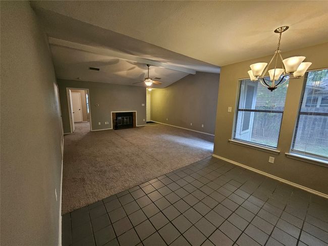 Unfurnished living room with lofted ceiling, baseboards, a glass covered fireplace, dark colored carpet, and ceiling fan with notable chandelier | Image 13