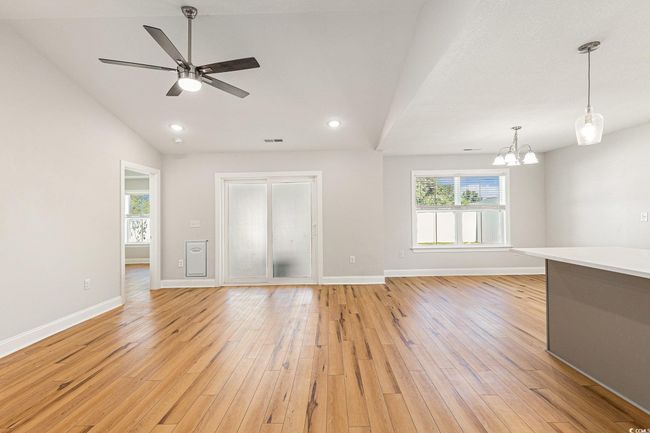 Unfurnished living room with a chandelier, light wood finished floors, vaulted ceiling, ceiling fan, and recessed lighting | Image 4