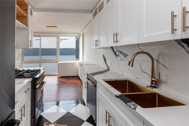 Kitchen with stainless steel appliances, white cabinetry, light stone countertops, glass insert cabinets, and a water view | Image 10